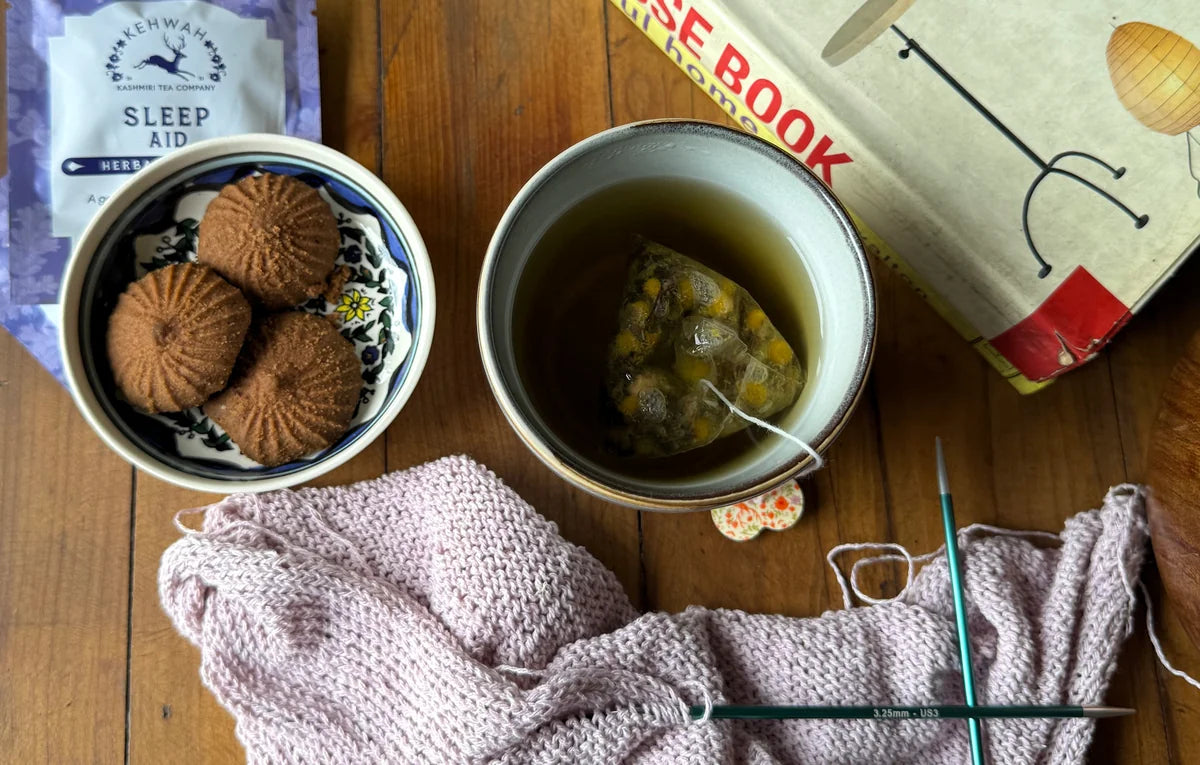 Sleep Aid in a mug beside a book, sachet and knitting