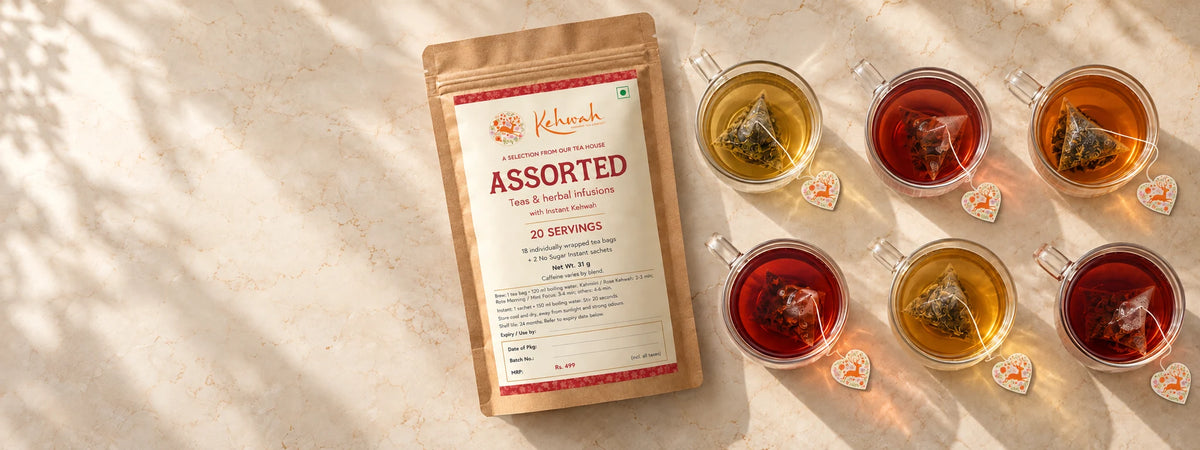 The brown Kehwah Assorted pouch surrounded by clear cups of golden and rose-coloured tea, with heart-shaped tags.
