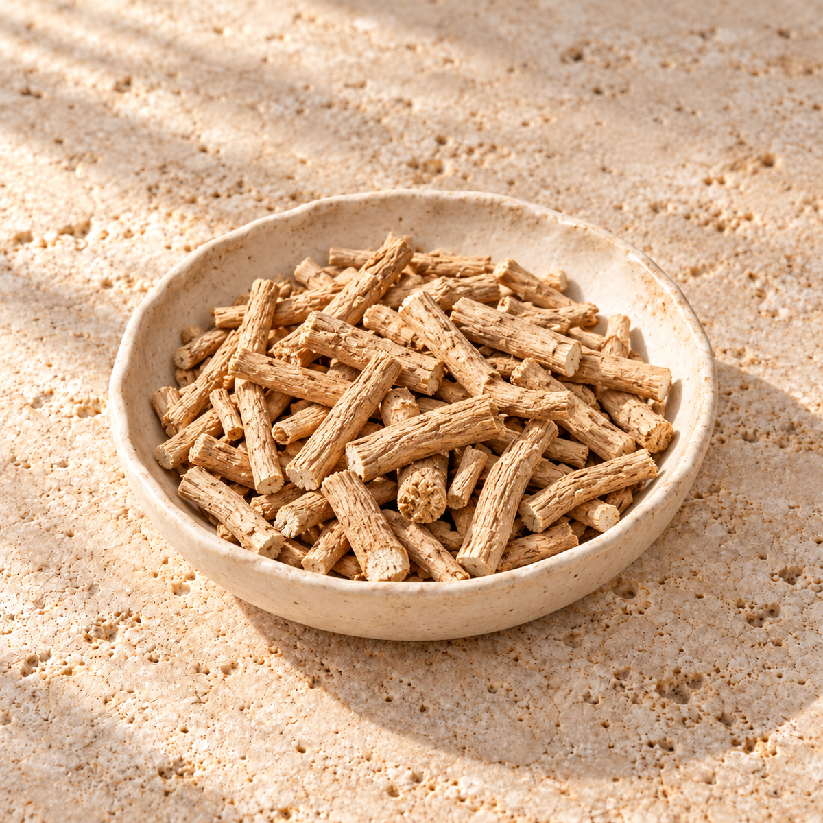 Dried ashwagandha roots with pale cut ends on warm limestone