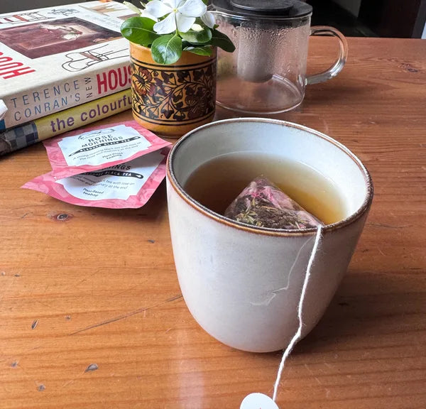 Rose Mornings steeping in a mug beside its sachet and flowers