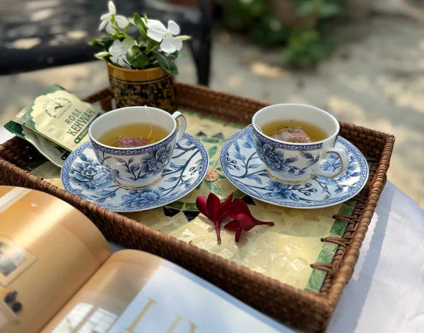 Two cups of Rose Kehwah on a mirrored tray beside rose petals