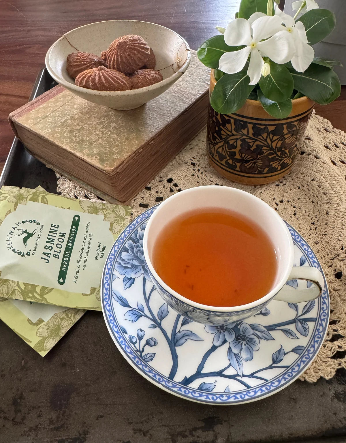 Amber Jasmine Rooibos in a blue and white cup with its sachet, biscuits and flowers