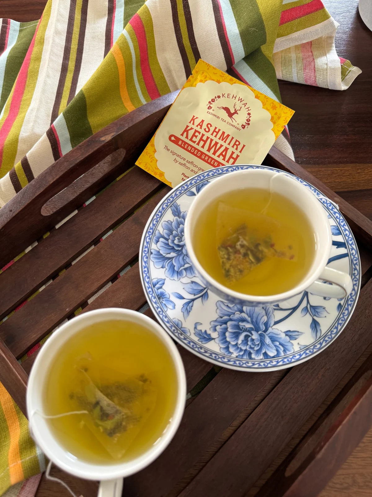 Two cups of Kashmiri Kehwah on a mirrored tray beside a woven scarf