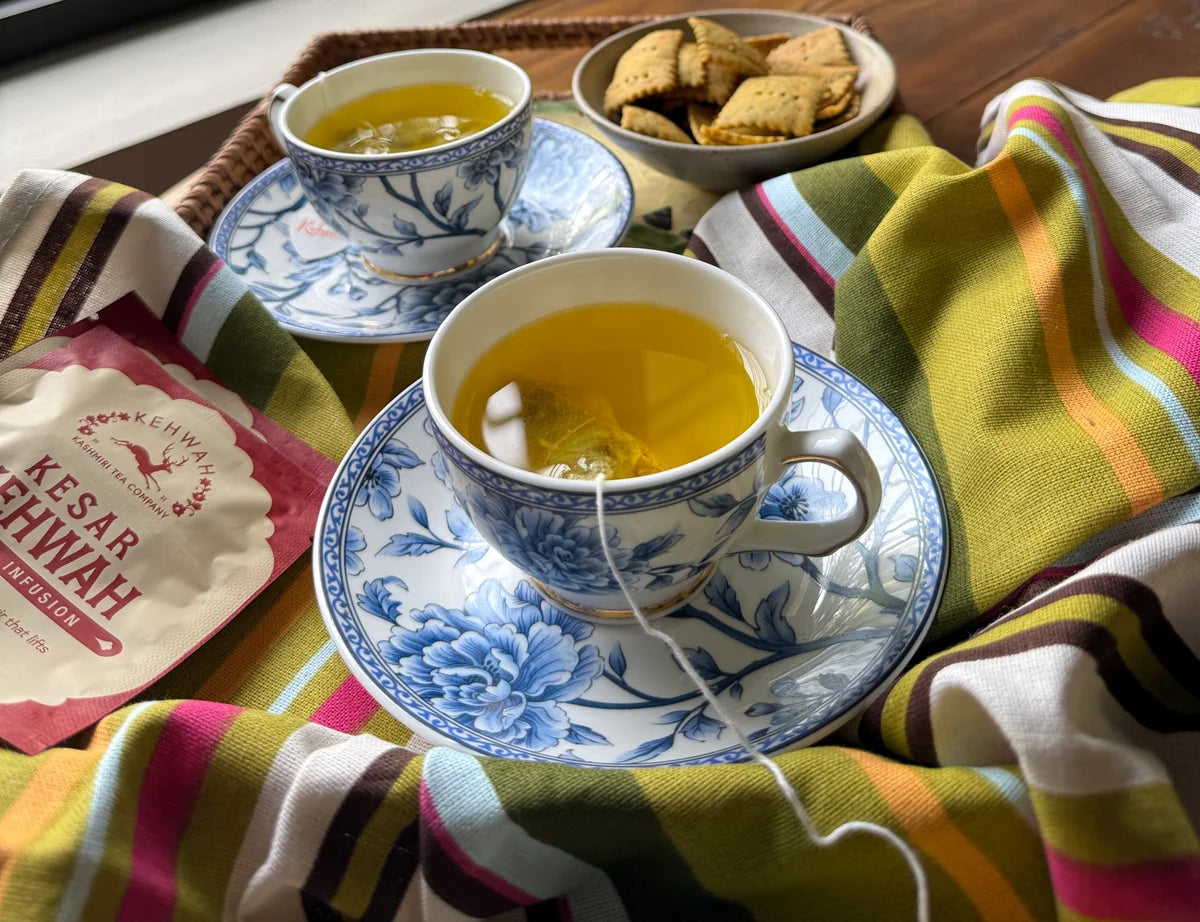 Two golden cups of Kesar Kehwah on a tray with the red sachet