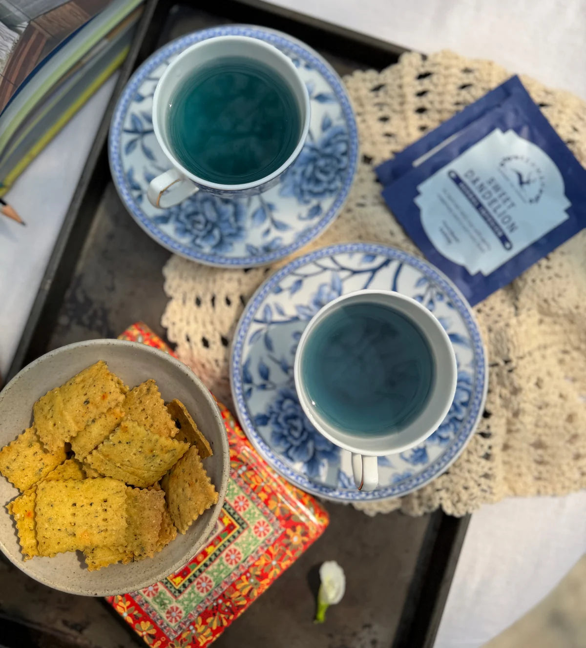 Two blue cups of Sweet Dandelion beside its sachet and a bowl of snacks
