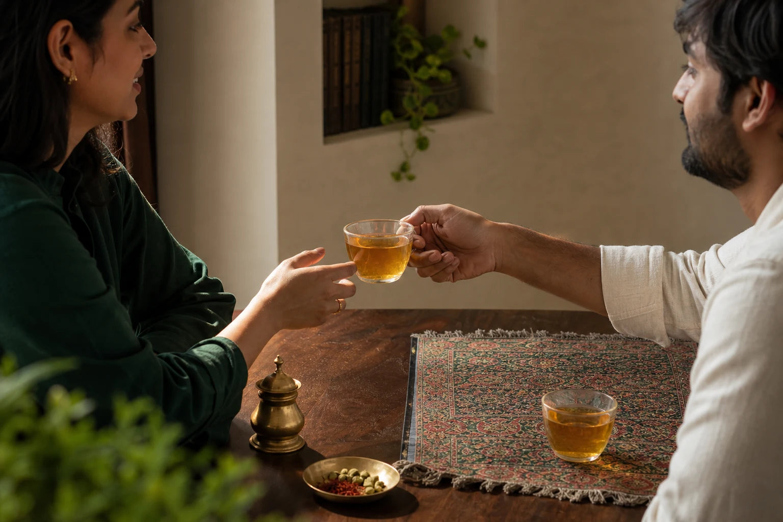Two adults sharing a clear saffron-gold cup at a warm family table